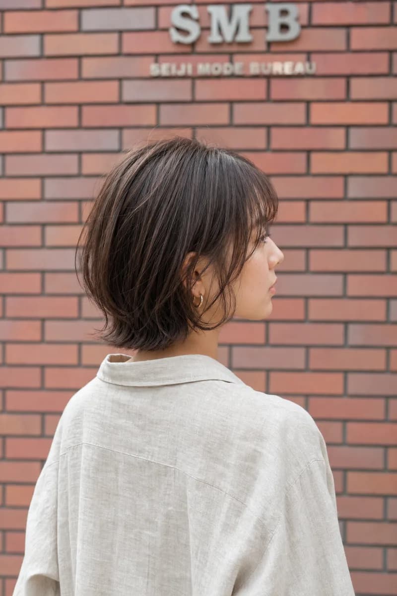 毛先を外にハネさせたショートボブの女性を斜め後ろから見た姿