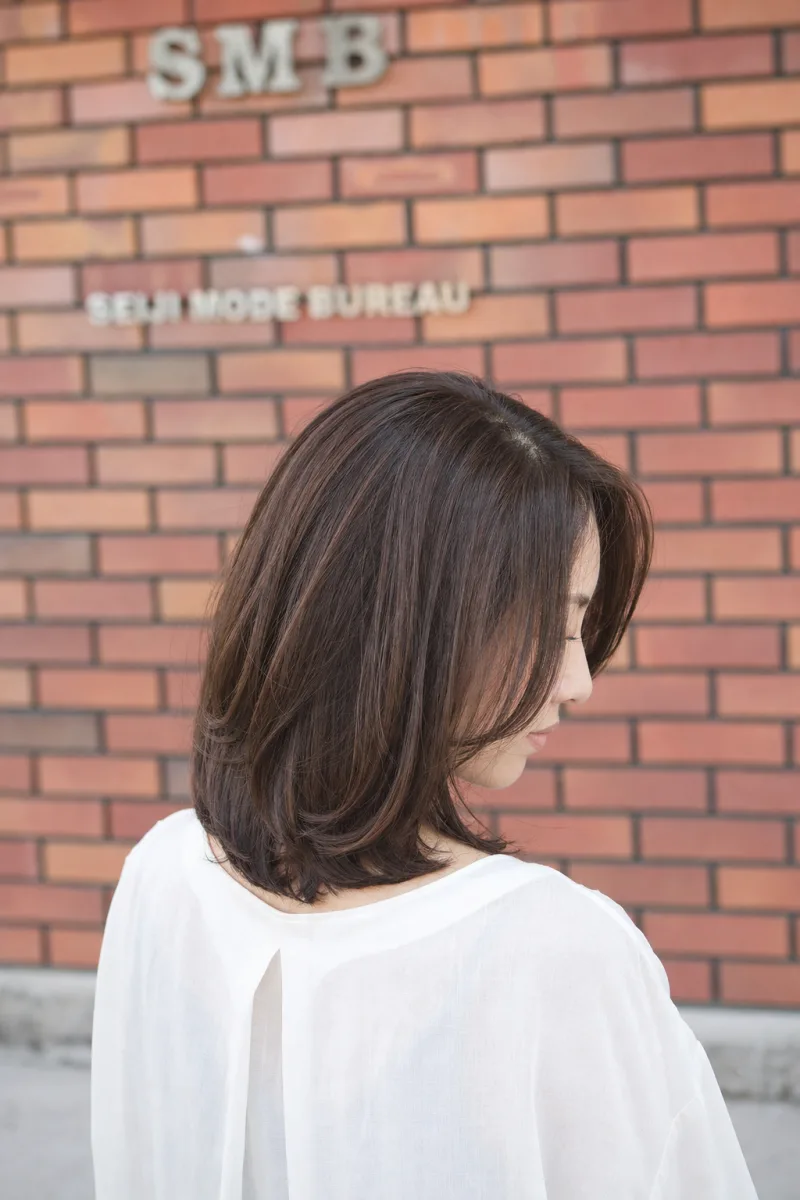 内側に流れるミディアムレイヤーの女性を斜め後ろから見た姿