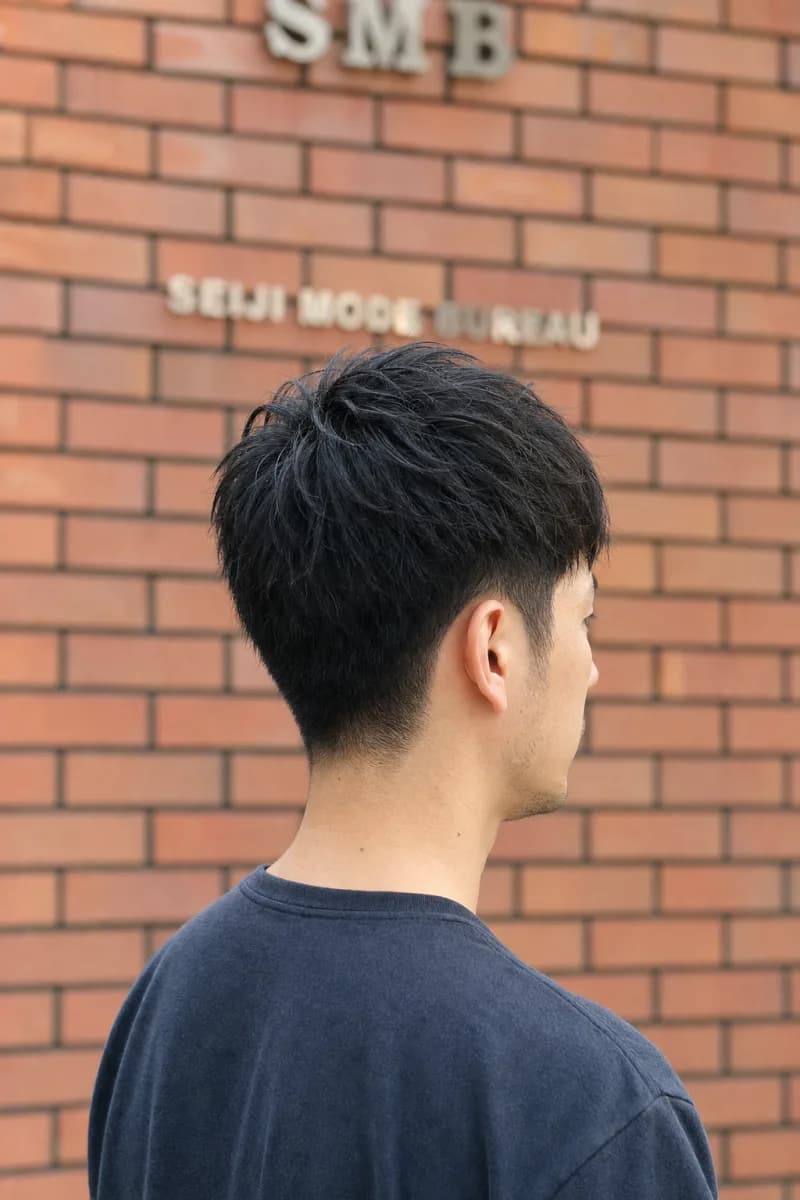 トップに束感を残したショートスタイルの男性を斜め後ろから見た姿