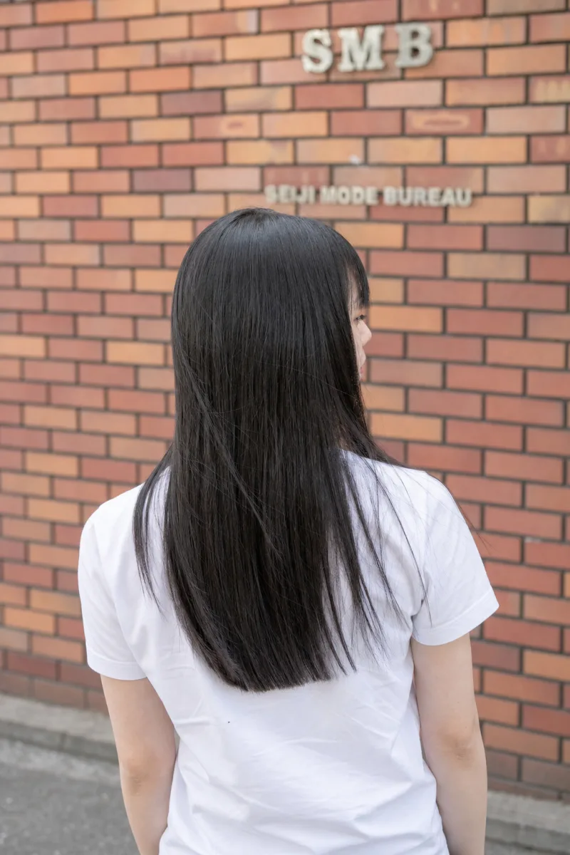 まっすぐ切りそろえた黒髪ロングが背中に流れる女性を後ろから見た姿